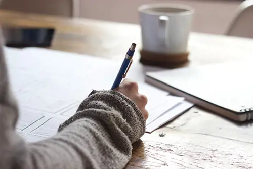 Person holding pen and writing on paper.