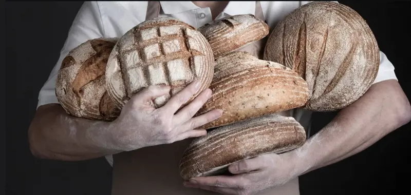 Man holding 6 loaves of freshly baked bread